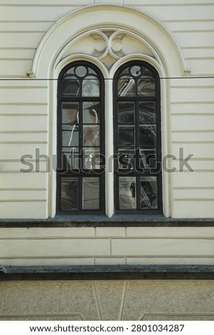 Front view of a double arched neo Gothic window with decorative stone molding details on a light beige historical building wall.