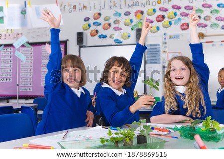 A front view of enthusiastic school kids raising their hands in excitement in a classroom
