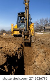 Front view of excavator digging deep trench in soil for foundation works. Heavy construction machinery shaping ground at outdoor building site.