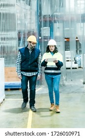 Front View Of Factory Workers Walking With Tablet At Plant. Confident Machine Operators Talking While Walking At Factory. Print Manufacturing Concept