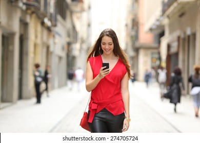 Front view of a fashion happy woman walking and using a smart phone on a city street