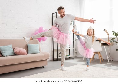 Front View Of Father And Daughter In Tutu Skirts Standing On One Leg