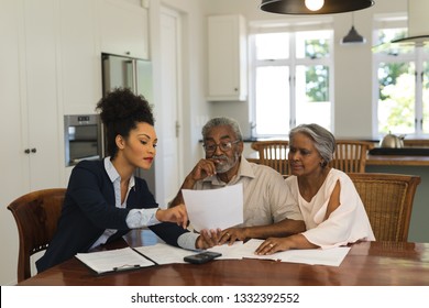 Front view of a female African American  real estate agent and senior couple discussing over documents at the table of the living room at home - Powered by Shutterstock