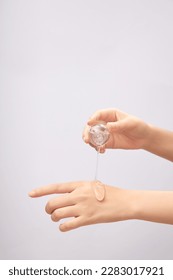 Front view of female hand pouring transparent essence on back of other hand on light background. Mockup scene for cosmetic product, daily skin care routine.
