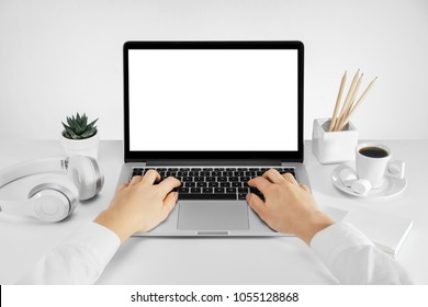 Front view of female hands working on laptop with blank white screen standing on the white office desk. Mock up, copy space for your text.