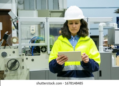 Front View Of Female Technician Holding Tablet. Confident Factory Worker Using Tablet While Standing Near Printing Machine. Print Manufacturing, Technology Concept