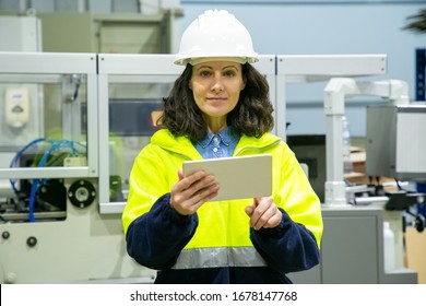 Front View Of Female Technician With Tablet Looking At Camera. Confident Factory Worker Using Tablet While Standing Near Printing Machine. Print Manufacturing, Technology Concept