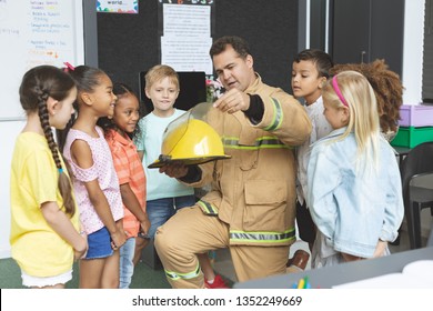 Front View Of Firefighter Teaching Student About Fire Safety While Holding Fire Helmet 