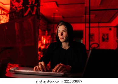 Front view of focused hacker man in black sweatshirt using laptop and desktop computer to breaking network system, from dark basement room with blue neon lights. Concept of data thief, internet attack - Powered by Shutterstock