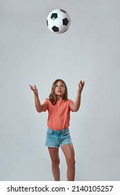 Front View Of Focused Little Girl Throwing Up Football Ball. Cute Caucasian Female Child Wearing Pink T-shirt And Jean Shorts. Childhood Concept. Isolated On White Background. Studio Shoot. Copy Space