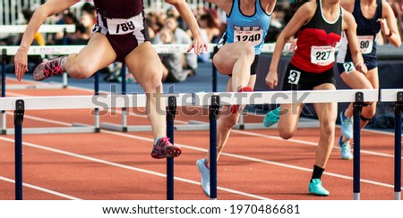 Front view of four high school girls running in a hurdle track and field race.