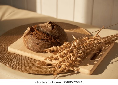 Front view of freshly baked rye bread on yeast-free starter and on mixture of whole grain, rye and wheat flour. It lies on cut board next to a dried flower with grains.Selective focus, sun.Copy space. - Powered by Shutterstock