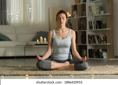 Front view full body portrait of a relaxed woman doing yoga exercise in the night at home with candles
