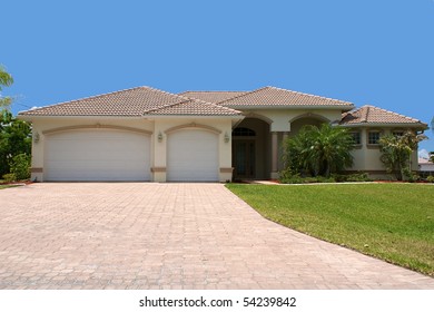 front view a generic florida home sits on a small grass covered hill with garage, palm trees and a clear blue sky, looking up the driveway.
