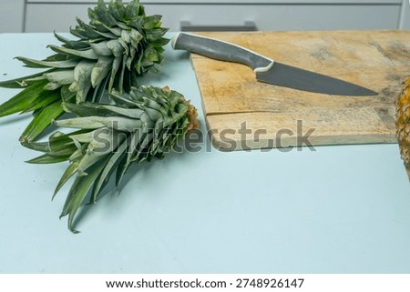 Front view of a generous amount of cut pineapple, covering a wooden board, with the knife placed next to the chunks.