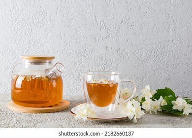 front view of a glass teapot with jasmine tea and a modern cup with a natural delicious drink. gray background. tea time - Powered by Shutterstock