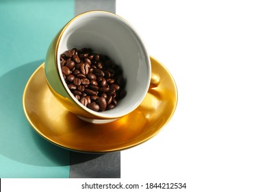 Front view for golden porcelain coffee cup copy with fresh roasted arabica beans. Large golden cup in antigravity position on the geometric grey and tiffany blue background.  - Powered by Shutterstock