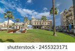 Front view of Grand Casino in Monte Carlo timelapse hyperlapse, Monaco. historical building and square with fountain and green grass. Palms on the side. Blue cloudy sky at summer day