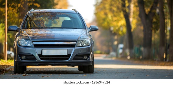Front view of gray shiny empty car parked in quiet area on wide alley under big trees on blurred green and yellow folliage bokeh background on bright sunny day. Transportation and parking concept. - Shutterstock ID 1236347524