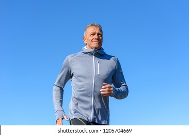 Front View Of Gray Smiling Man Wearing Sportswear Running Along River In A Low Angle View