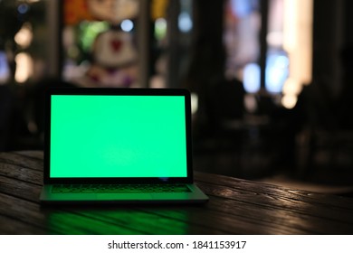 Front View Of Green Screen Laptop Computer At Dark Night. Defocused Lights Background