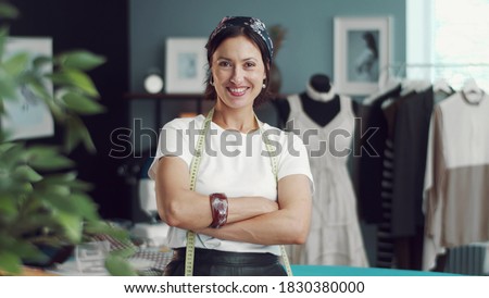 Front view of grinning female dressmaker with arms crossed standing in sewing workshop looking at camera