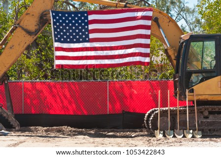 Front view of a ground breaking ceremony for a county park in a tropical setting with the american flag, ceremonial shovels, heavy equipment and pollution control fencing