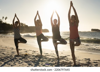 Front View Of A Group Of Caucasian Female Friends Enjoying Free Time On A Beach On A Sunny Day, Practicing Yoga 