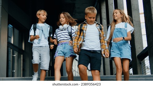 Front view of group of four attractive caucasian schoolchildren walking together down the stairs in college campus talking and laughing with joy. Education and school children life concept - Powered by Shutterstock