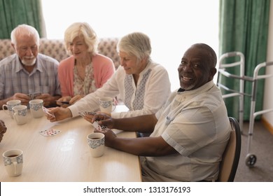 Front view of group of happy senior people playing cards in living room at nursing home - Powered by Shutterstock