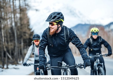 Front view of group of mountain bikers riding on road outdoors in winter.