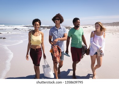 Front view of a group of multi ethnic friends walking side by side on the beach and smiling in the sunshine