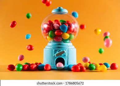 front view of a handful of gummy sweets with a candy machine dispenser, colors red, yellow, green, blue and pink.