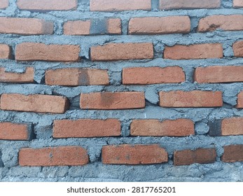 Front view of a handmade red brick wall with cement mortar. Rustic brick texture background for architecture and construction projects.