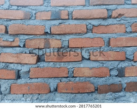 Front view of a handmade red brick wall with cement mortar. Rustic brick texture background for architecture and construction projects.