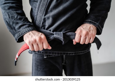 Front view of hands of unknown caucasian man in kimono gi standing while holding and tie knot black bjj belt brazilian jiu jitsu concept copy space - Powered by Shutterstock