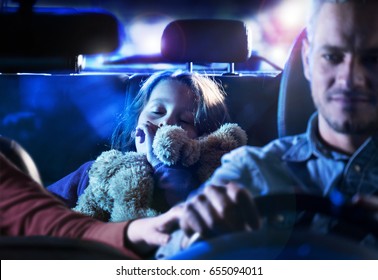 Front View. Handsome Man Driving His Car At Night. At The Back, His Little Girl Fell Asleep With Her Teddy In Her Arms