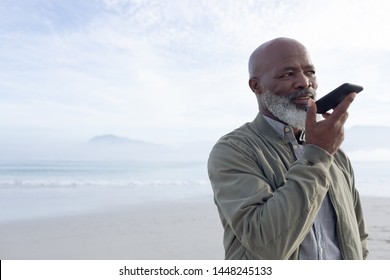 Front view of handsome senior African-American man talking on mobile phone while standing on the beach on beautiful day with mountains in the background. Authentic Senior Retired Life Concept - Powered by Shutterstock