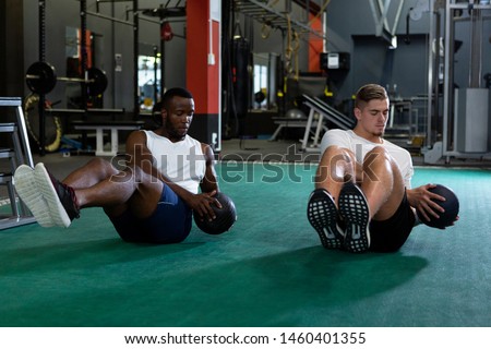 Front view of handsome young diverse male athletics exercising together with exercise ball in fitness center. Bright modern gym with fit healthy people working out and training