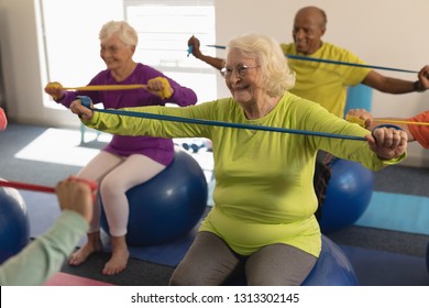 Front View Of Happy Active Senior People Exercising With Resistance Band In Fitness Studio