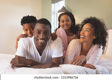 Front view of happy African American family lying on bed and looking at camera in a comfortable home. Social distancing and self isolation in quarantine lockdown for Coronavirus Covid19 - Powered by Shutterstock