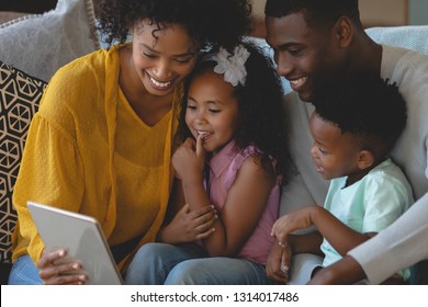 Front view of happy African American parents with their cute children using digital tablet on sofa. Social distancing and self isolation in quarantine lockdown for Coronavirus Covid19
