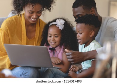 Front view of happy African American parents with their cute children using laptop on sofa. Social distancing and self isolation in quarantine lockdown for Coronavirus Covid19
