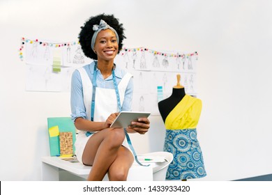 Front view of happy African american female fashion designer using digital tablet on table in office
