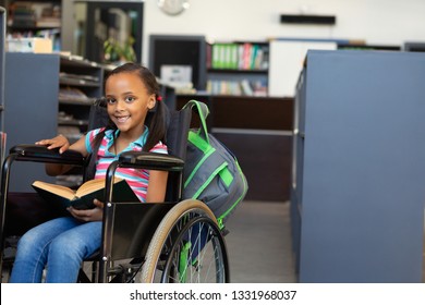 Front view of a happy disabled mixed-race schoolgirl reading a book in the classroom at school - Powered by Shutterstock