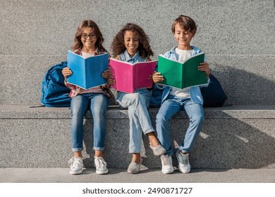 Front view of happy diverse multiethnic group school kids pupils classmates friends with backpacks holding colorful notebooks in hands having fun outdoors sitting on the stairs steps in background - Powered by Shutterstock