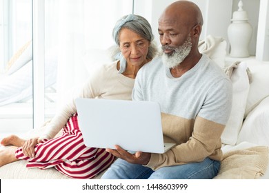 Front view of happy diverse senior couple using laptop on sofa in beach house. Authentic Senior Retired Life Concept - Powered by Shutterstock