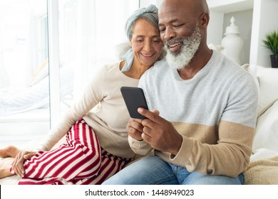 Front view of happy diverse senior couple using a smartphone on sofa in beach house. Authentic Senior Retired Life Concept - Powered by Shutterstock