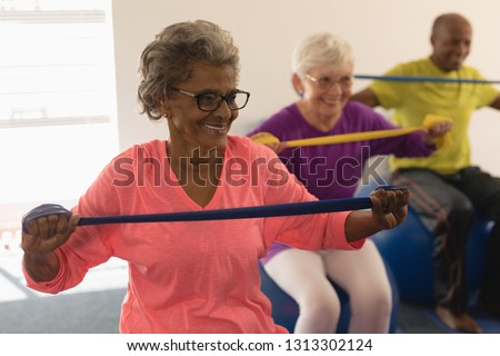 Front view of happy diverse senior woman exercising with resistance band in fitness studio
