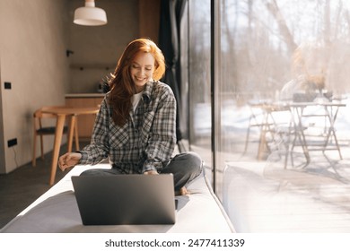 Front view of happy freelancer female remote working on laptop computer sitting on wide windowsill with nature view on sunny day. Smiling young businesswoman typing on keyboard looking to screen. - Powered by Shutterstock